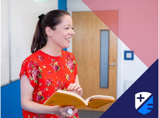 Teacher Lynda Moloney speaking in front of a whiteboard book in hand