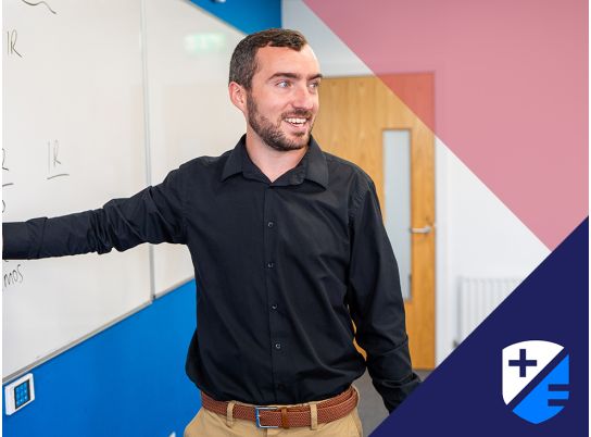 Teacher Patrick points at whiteboard while speaking to class